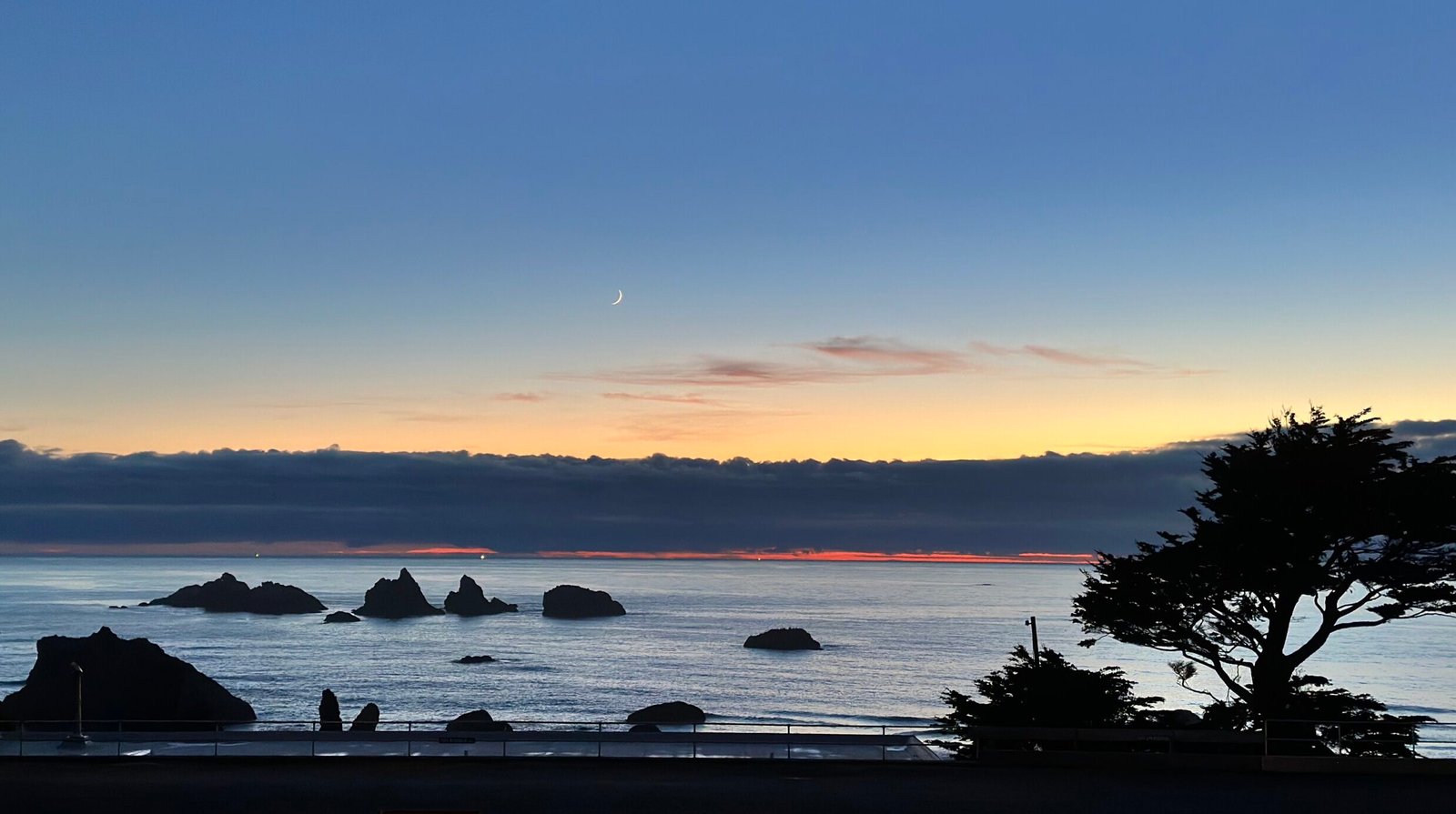A wide ocean horizon at the threshold of light, with distant land visible in soft silhouette.